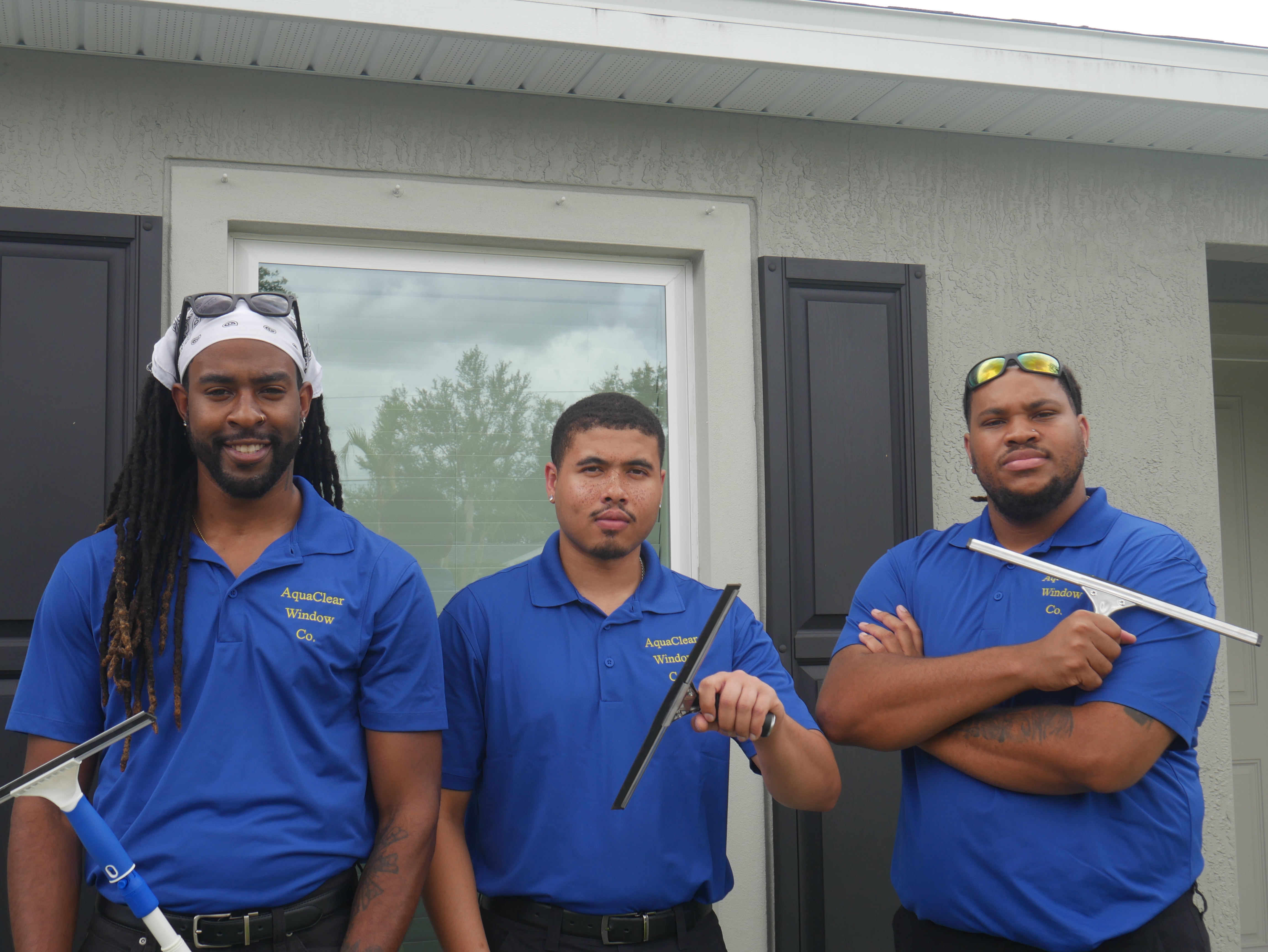 AquaClear Window Co. team members holding window cleaning equipment in front of a home